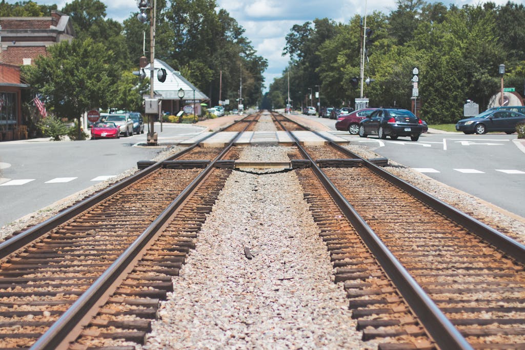 Railroad tracks intersecting through a charming small town with cars and trees.